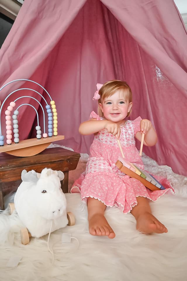 little girl in a pink dress sitting on the floor playing with a white moose and rainbow abacus