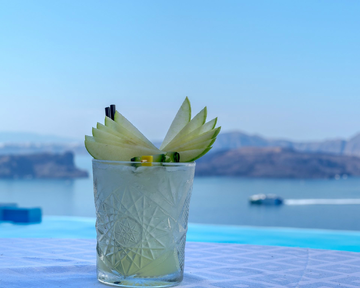 picture of a cocktail (which and yellow) with flower or fruit on a table with a blurred background of the sea and a boat sailing across the ocean