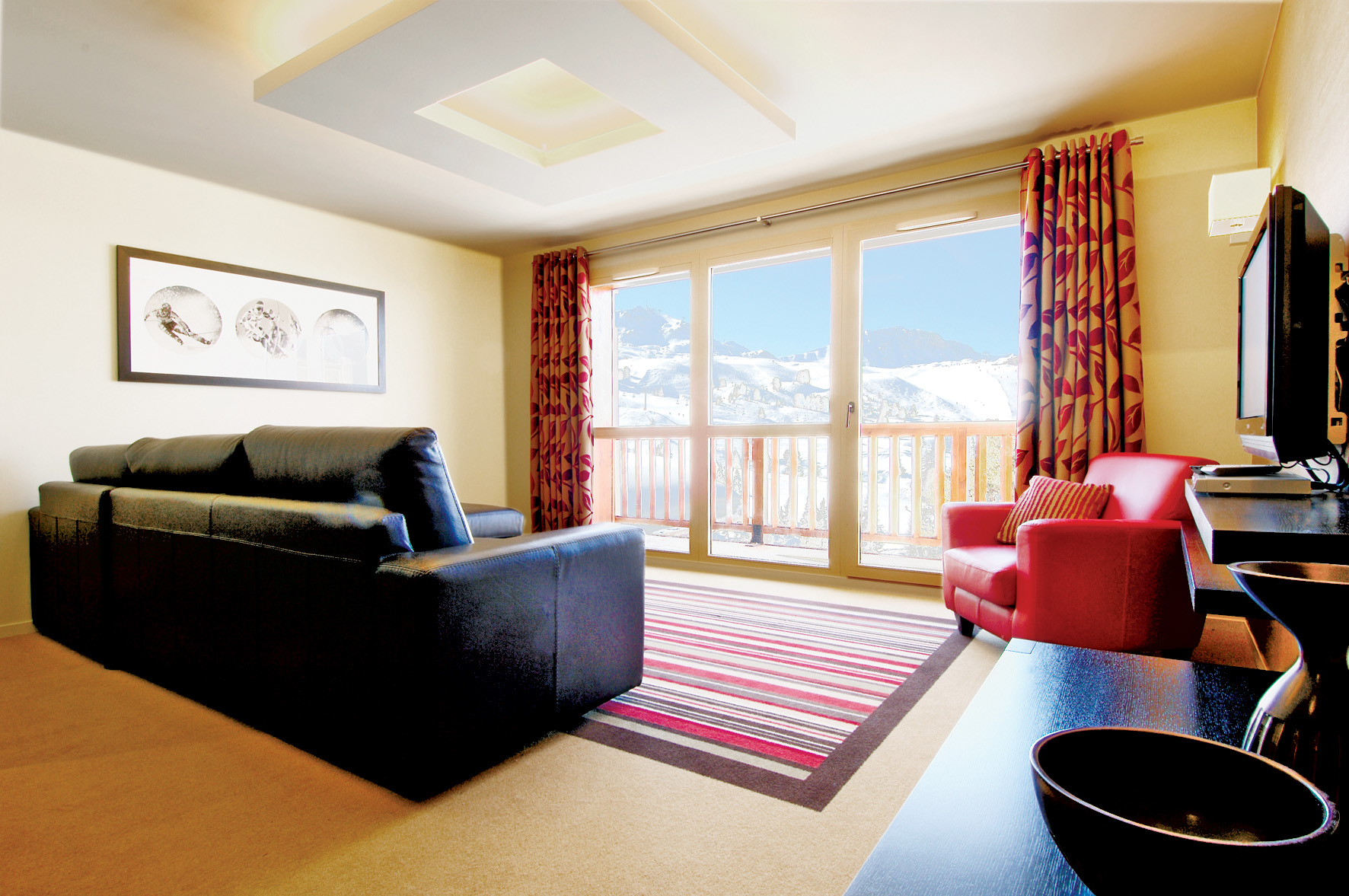 view of the lounge with red and beige curtains, leather sofa, red chair, striped rug facing towards floor to ceiling sliding door overlooking the ski slopes/mountains