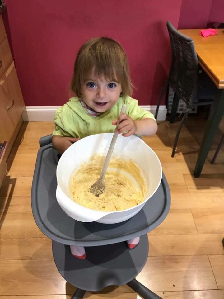 Toddler sitting in her highchair with a mixing bowl making cakes