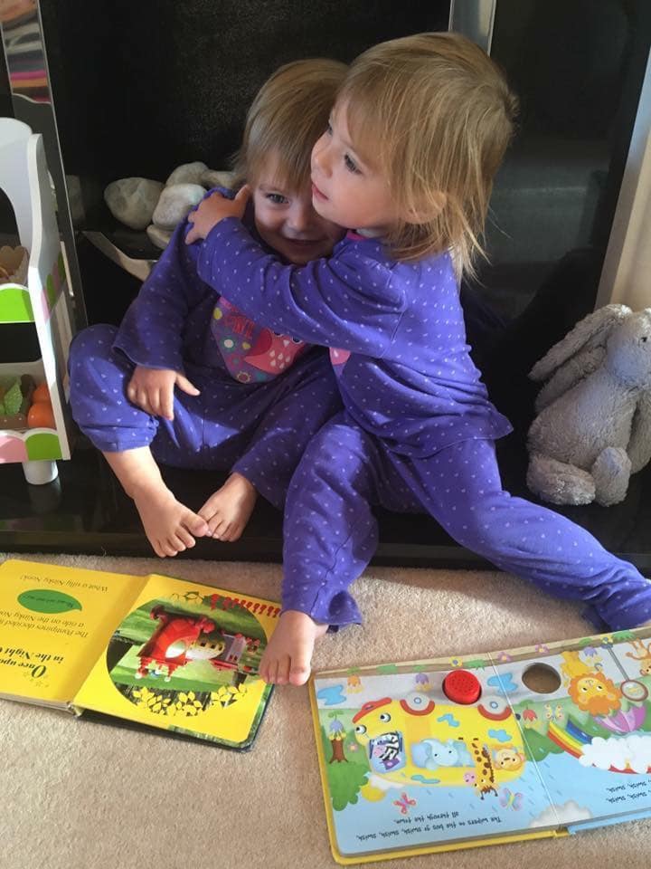 two toddlers sitting on the floor reading books together