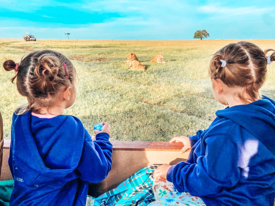 two girls sitting in the safari jeep watching lions sleeping in the grass