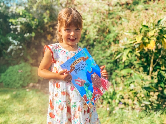 Little girl holding a personalised story book about pirates in the garden