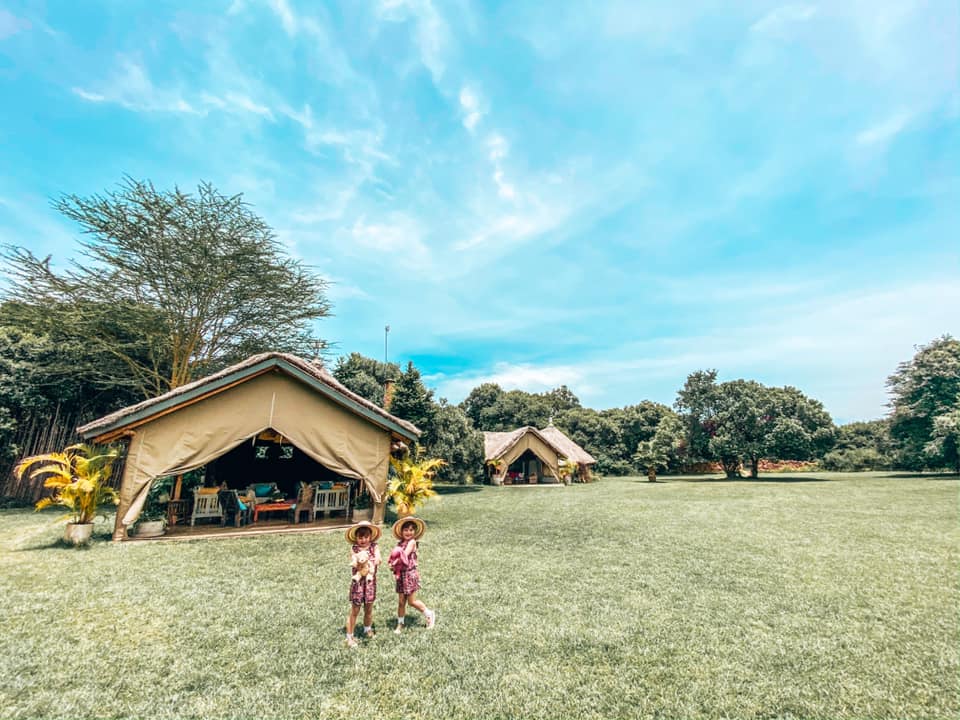 twins wearing hats stood outside a hut on grass in the house in the wild grounds