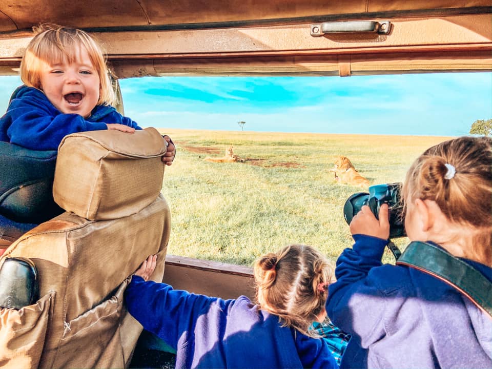 Best Time to Visit Africa - three children looking out of the safari jeep in Kenya. They are looking at Lions in the distance