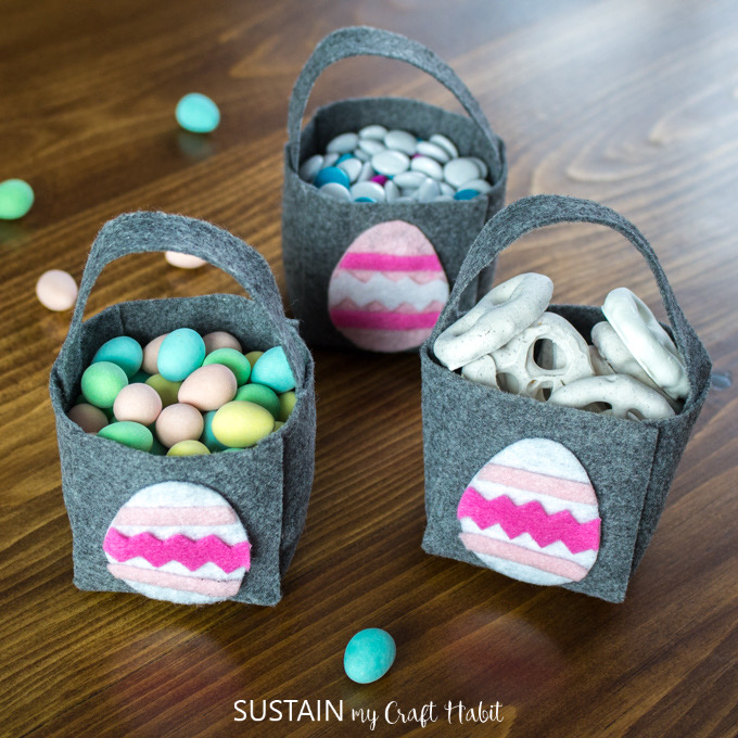 three felt Easter baskets with pink felt Easter eggs on the front filled with sweets