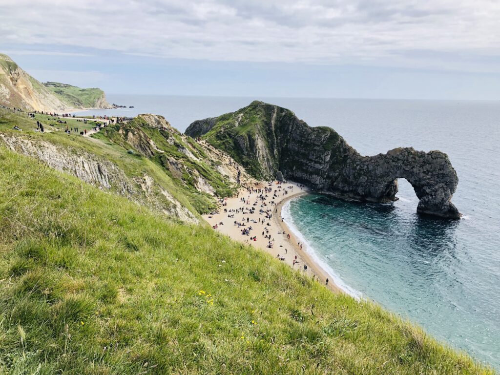 large hill rolling down to the beach with is full of visitors playing and walking along the coastal path