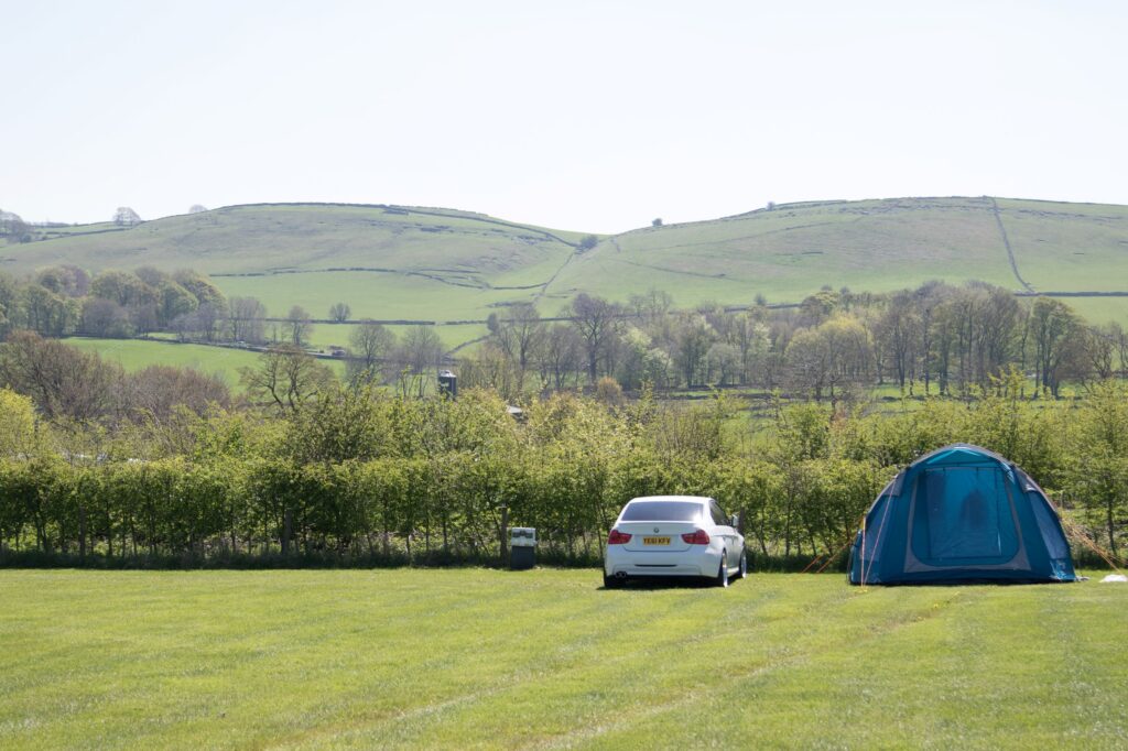 wide open field with a blue tent to the right and a white car next to it