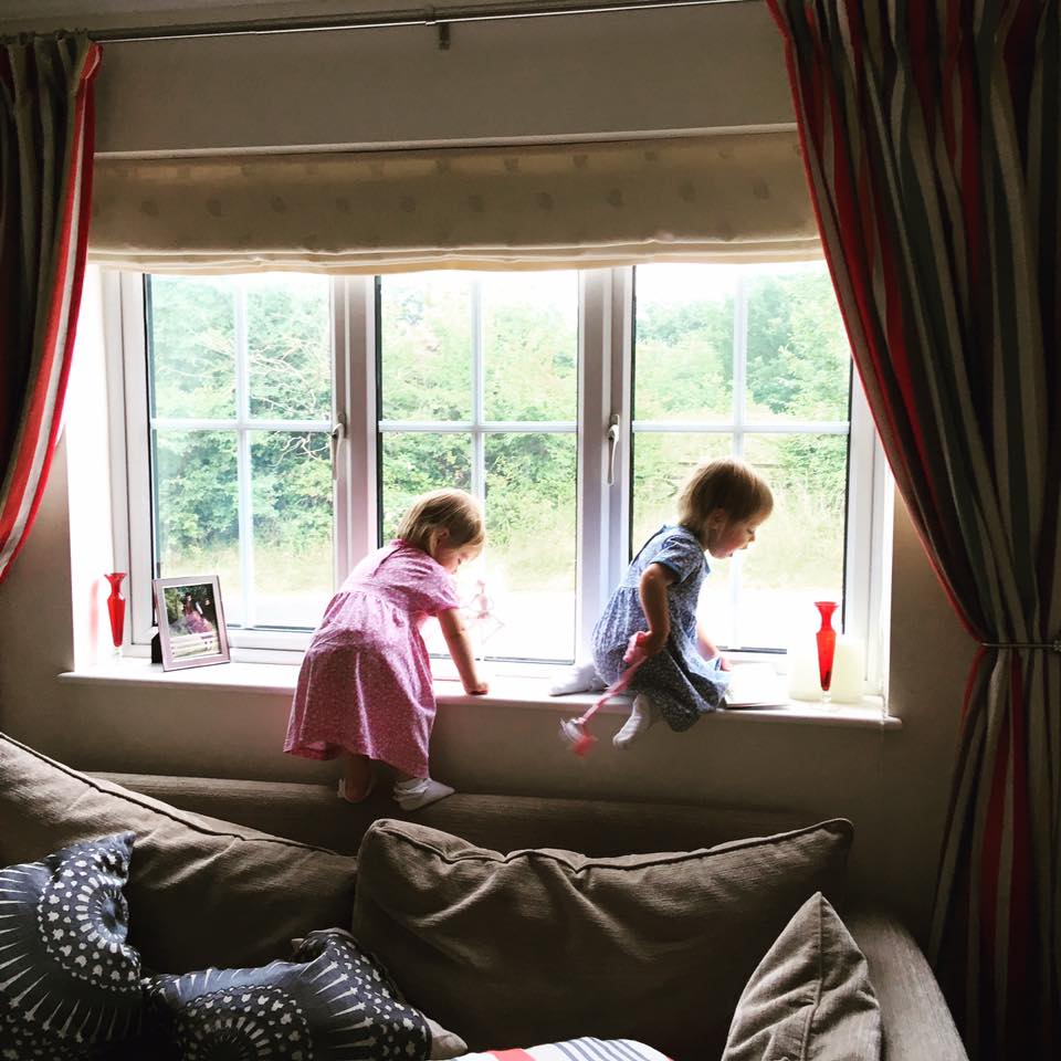 two girls climbing on the back of the sofa looking out of the window