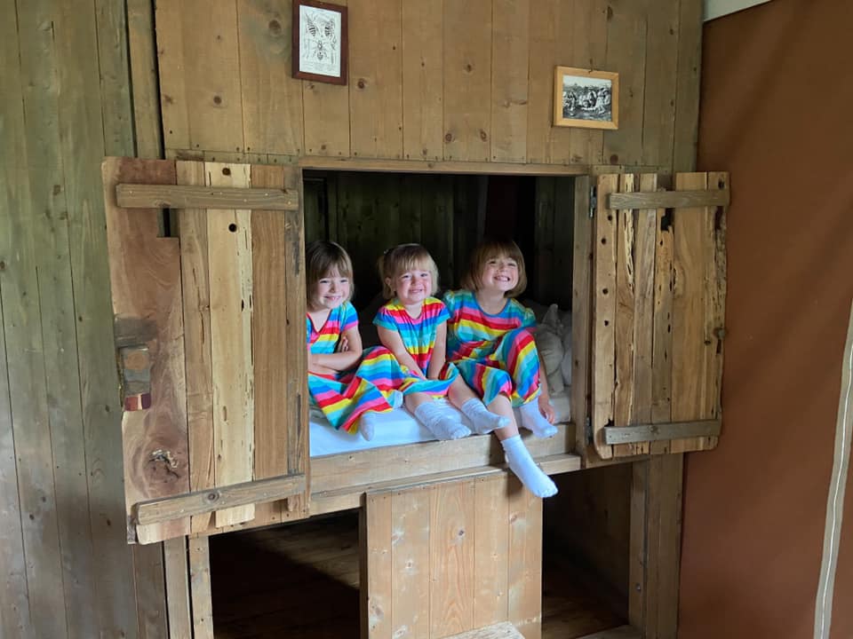 three children in rainbow dresses sitting in the cupboard bed at feather down glamping lodge