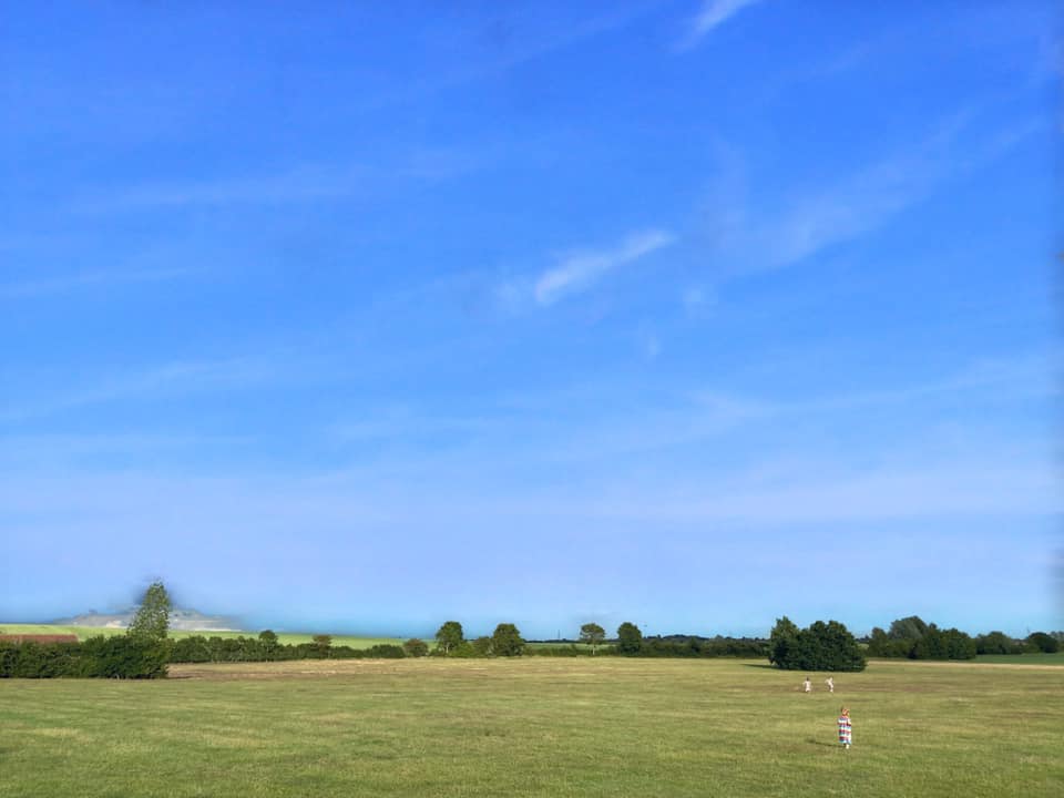 green fields and blue sky with children running in the distance