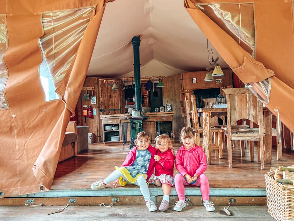 three children sitting in the opening of a glamping tent