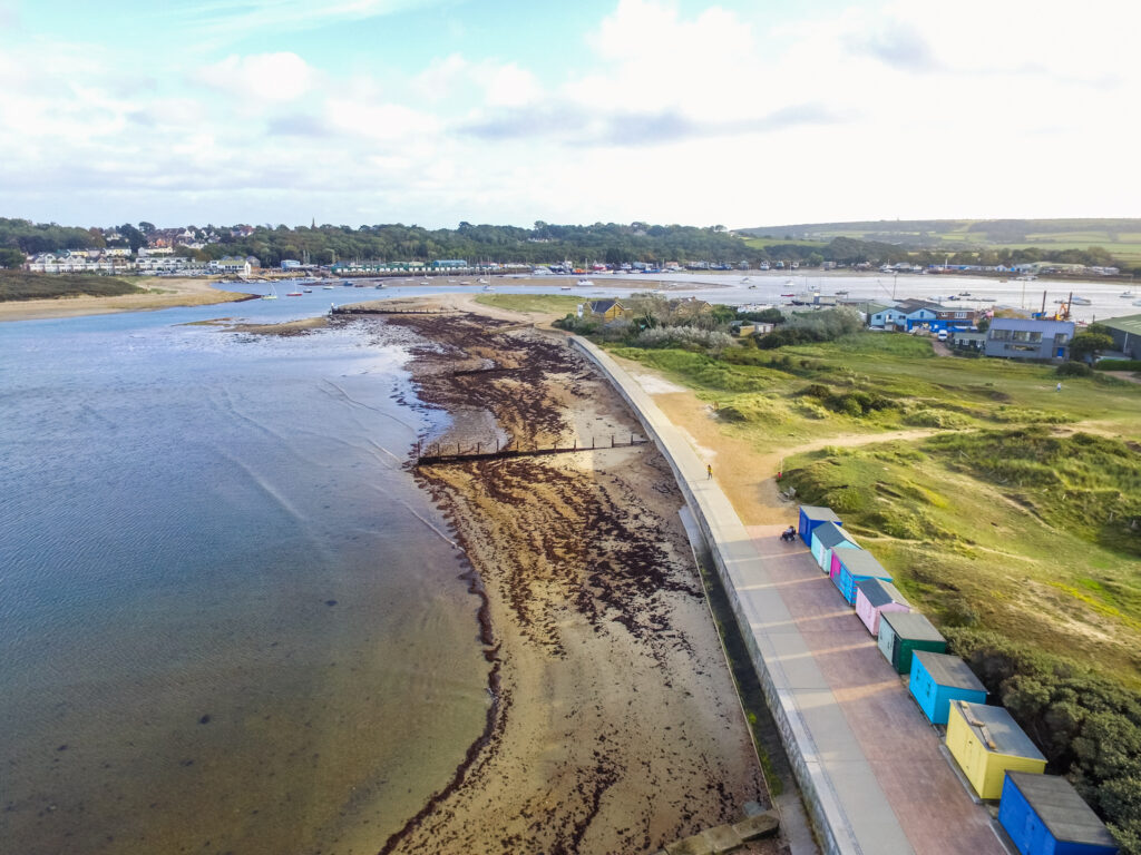 aerial view of beach and grassland with colourful beach huts to one end