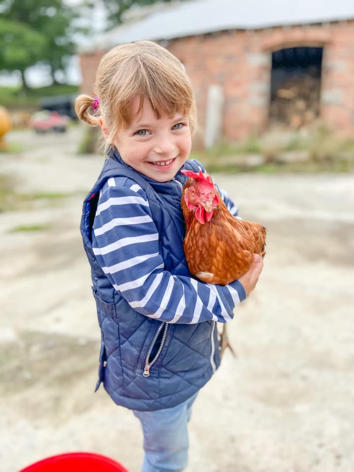 Young girl wearing a blue and white jumper, smiling holding a chicken