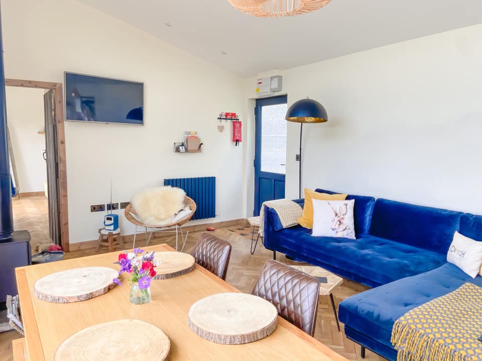 Lounge area at Penlan with a navy velvet L shaped sofa, and wooden table with log type place mats