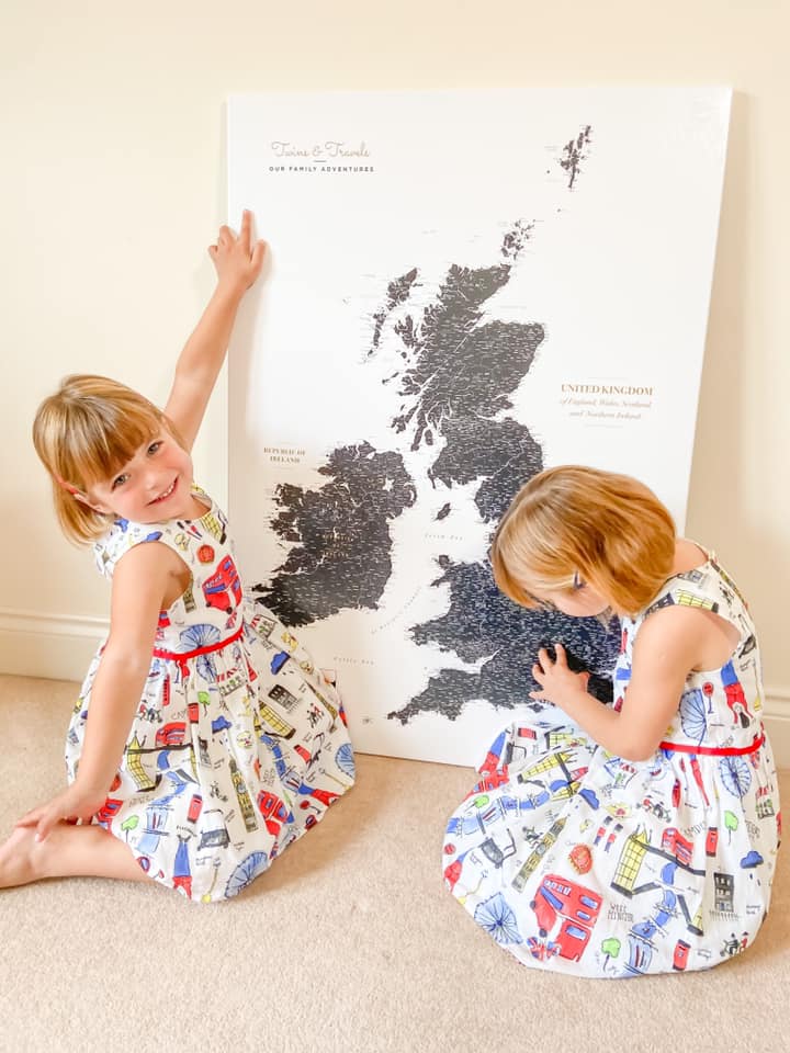 large trip map on the floor with a girl pointing to the map, and the other pinning it