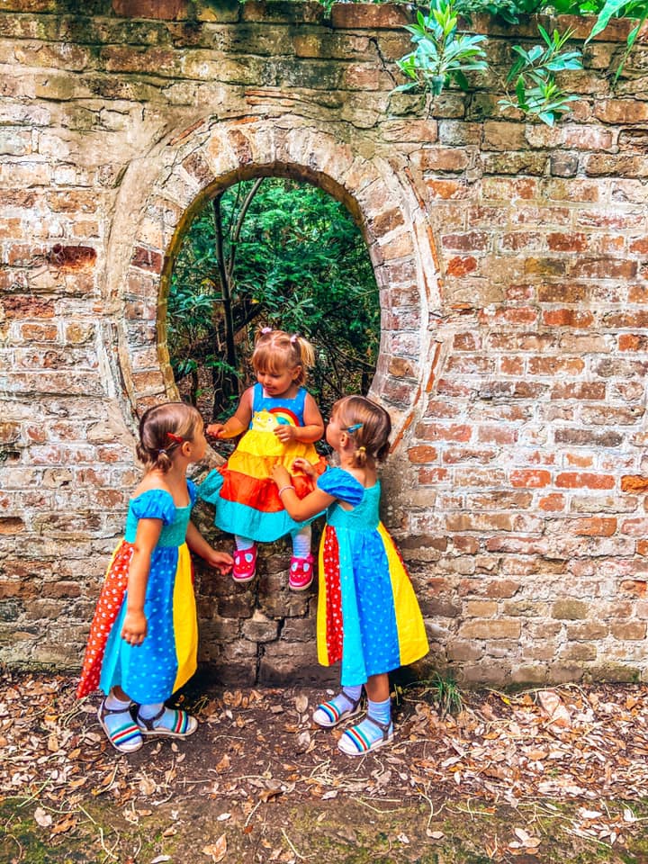 three children in bright dresses with one child sitting on a brick wall