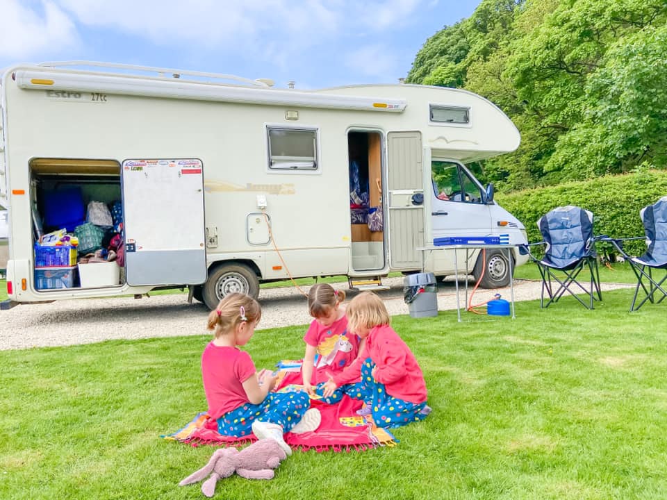 three girls playing on the picnic blanket with motorhome in the background