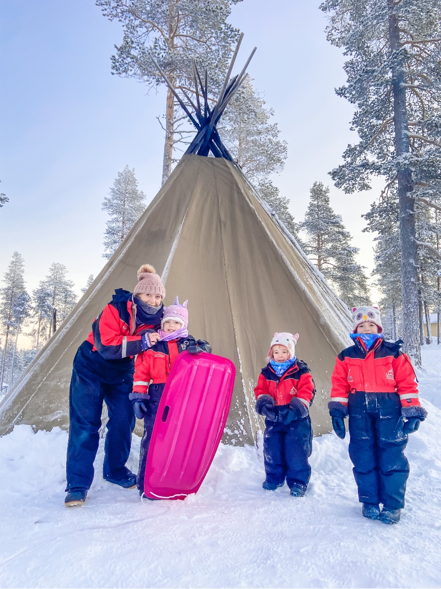 three young girls and a lady standing in the snow outside a tipi - Lapland Holiday