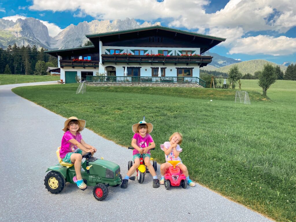 Summer in Austria children on ride ons in front of ski chalet