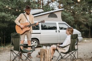Man playing the guitar to a woman outside a camper van